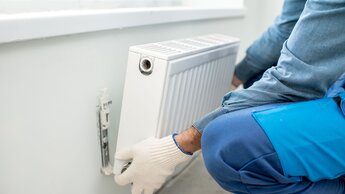 Handwerker bei der Montage eines Heizkörpers an der weißen Wand im Innenbereich, Nahaufnahme | © Adobe Stock